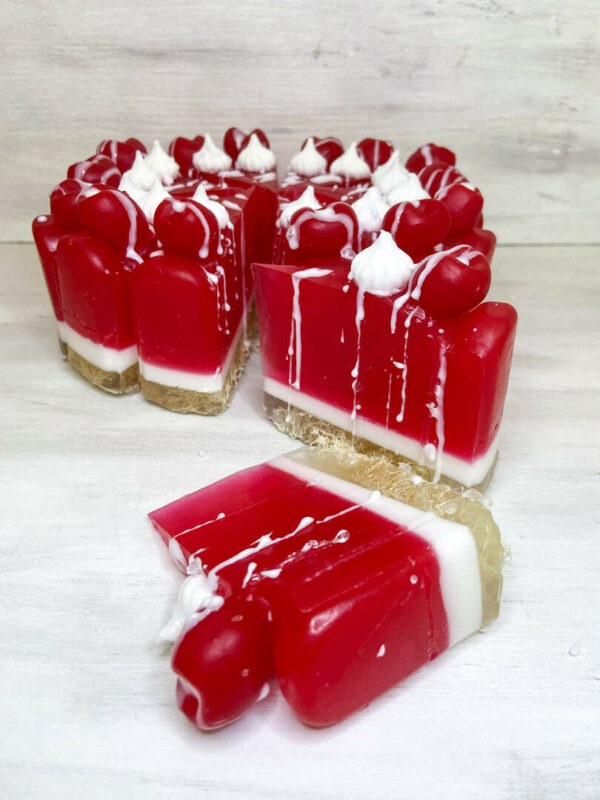 Χειροποίητη τούρτα σαπουνιού σε μορφή cheesecake με αποχρώσεις κερασιού και λευκού, διακοσμημένη με ρεαλιστικά στοιχεία και έντονο άρωμα κερασιού.