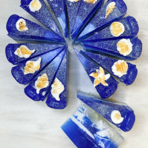 Χειροποίητη τούρτα σαπουνιού Ocean με βαθύ μπλε χρώμα, λευκά κυματιστά σχέδια και διακόσμηση από σαπουνένια κοχύλια.